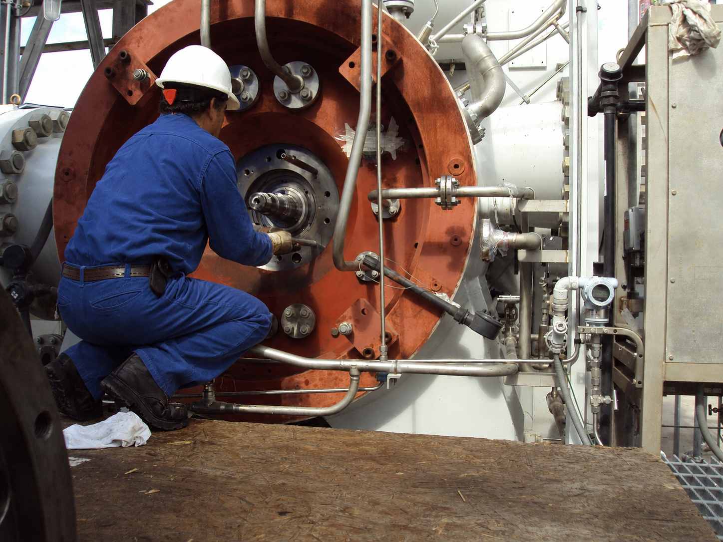Field service specialist in blue coveralls inspecting compressor machinery